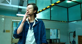Movie still from “Bronson” (2008), directed by Nicolas Winding Refn – A man smoking a cigarette while standing in a building; Medium shot, Low angle