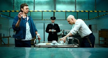 Movie still from “Bronson” (2008), directed by Nicolas Winding Refn – Two men in a kitchen and a man in a police uniform; Medium shot, Low angle