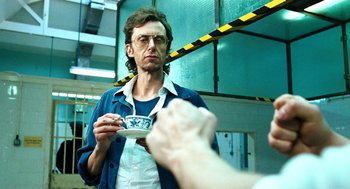 Movie still from “Bronson” (2008), directed by Nicolas Winding Refn – A man holding a coffee cup in front of a mirror; Close Up shot, Over the shoulder angle