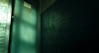 Movie still from “Bronson” (2008), directed by Nicolas Winding Refn – A dark room with a brick wall and a light shining on the wall; Medium shot, Low angle
