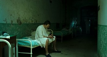 Movie still from “Bronson” (2008), directed by Nicolas Winding Refn – A man sitting on a hospital bed looking at his cell phone; Wide shot, High angle
