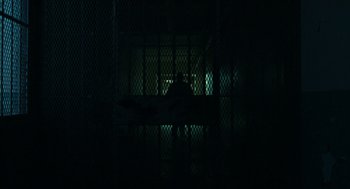 Movie still from “Bronson” (2008), directed by Nicolas Winding Refn – A person standing in a dark room behind a fence; Extreme Wide shot, Low angle