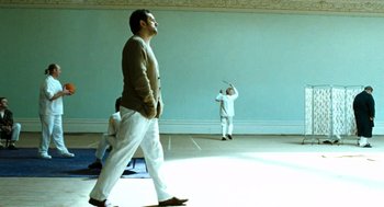 Movie still from “Bronson” (2008), directed by Nicolas Winding Refn – A man standing in front of another man holding a baseball bat; Wide shot, Low angle