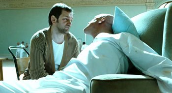 Movie still from “Bronson” (2008), directed by Nicolas Winding Refn – A man sitting next to another man in a hospital bed; Medium shot, Over the shoulder angle