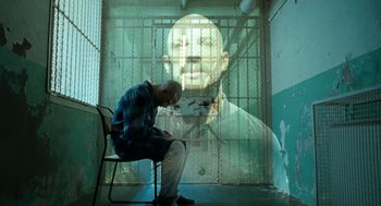 Movie still from “Bronson” (2008), directed by Nicolas Winding Refn – A man sitting on a chair in front of a prison cell; Medium shot, Low angle