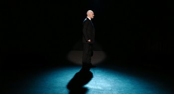 Movie still from “Bronson” (2008), directed by Nicolas Winding Refn – A man in a black suit standing in a dark room; Wide shot, Low angle