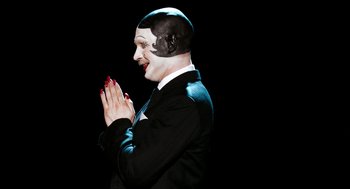 Movie still from “Bronson” (2008), directed by Nicolas Winding Refn – A mime in a black suit clapping his hands; Close Up shot, High angle