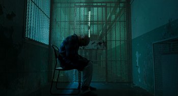 Movie still from “Bronson” (2008), directed by Nicolas Winding Refn – A man sitting on a chair in a jail cell; Wide shot, High angle