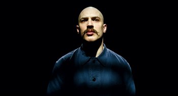 Movie still from “Bronson” (2008), directed by Nicolas Winding Refn – A bald man with a mustache is posing for a picture; Close Up shot, Low angle