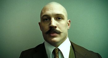 Movie still from “Bronson” (2008), directed by Nicolas Winding Refn – A bald man with a mustache wearing a suit and tie; Close Up shot, Low angle