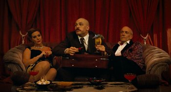 Movie still from “Bronson” (2008), directed by Nicolas Winding Refn – A man sitting on top of a briefcase next to two other people; Medium shot, Low angle