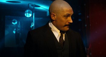 Movie still from “Bronson” (2008), directed by Nicolas Winding Refn – A man with a bald head in a suit and tie; Close Up shot, Over the shoulder angle