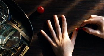 Movie still from “Bronson” (2008), directed by Nicolas Winding Refn – A hand with red nails reaching for an object on a table; Extreme Close Up shot, Overhead angle