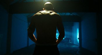 Movie still from “Bronson” (2008), directed by Nicolas Winding Refn – A man with his hands on his hips in a dark room; Medium shot, Low angle