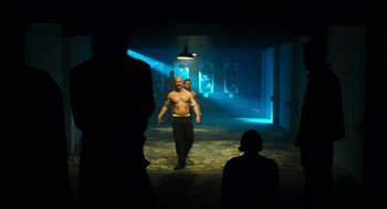Movie still from “Bronson” (2008), directed by Nicolas Winding Refn – A man walking down a hallway in the dark; Wide shot, Low angle