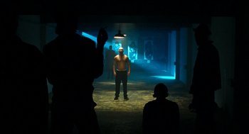 Movie still from “Bronson” (2008), directed by Nicolas Winding Refn – A man standing in a dark room with a light shining on him; Wide shot, Low angle