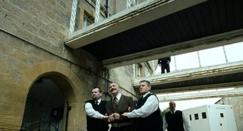 Movie still from “Bronson” (2008), directed by Nicolas Winding Refn – A group of men standing next to each other in a building; Wide shot, Low angle