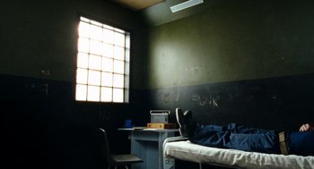 Movie still from “Bronson” (2008), directed by Nicolas Winding Refn – A room with a bed , desk , chair and a window; Wide shot, High angle