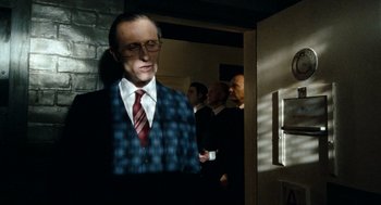 Movie still from “Bronson” (2008), directed by Nicolas Winding Refn – A man in a suit and tie standing in a room; Medium shot, Low angle