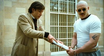 Movie still from “Bronson” (2008), directed by Nicolas Winding Refn – A man in a suit is handing a baseball bat to another man; Medium shot, Over the shoulder angle