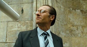 Movie still from “Bronson” (2008), directed by Nicolas Winding Refn – A man in a suit and tie standing in front of a building; Close Up shot, Low angle