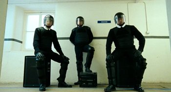 Movie still from “Bronson” (2008), directed by Nicolas Winding Refn – A group of men in black suits and helmets; Wide shot, Low angle