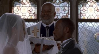 Movie still from “Brown Sugar” (2002), directed by Rick Famuyiwa – A man in a suit and tie holding a cross; Medium shot, High angle