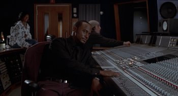 Movie still from “Brown Sugar” (2002), directed by Rick Famuyiwa – A man sitting in front of a sound board; Medium shot, Over the shoulder angle