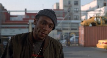 Movie still from “Brown Sugar” (2002), directed by Rick Famuyiwa – A man in a hat and jacket standing on a street; Close Up shot, Over the shoulder angle