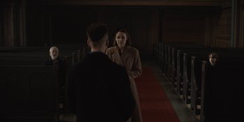 Movie still from “Dark” (2017), created by Baran bo Odar – A man and a woman are standing in front of pews in a church; Medium shot, Over the shoulder angle