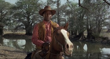 Movie still from “Buck and the Preacher” (1972), directed by Joseph Sargent – A man riding on the back of a brown horse; Medium shot, Low angle
