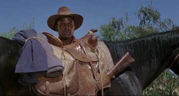 Movie still from “Buck and the Preacher” (1972), directed by Joseph Sargent – A man in a cowboy hat and a saddle; Medium shot, Low angle