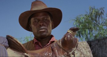 Movie still from “Buck and the Preacher” (1972), directed by Joseph Sargent – A man wearing a cowboy hat holding a saddle; Close Up shot, Low angle