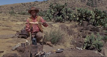 Movie still from “Buck and the Preacher” (1972), directed by Joseph Sargent – A man in a hat is holding a wooden stick; Medium shot, High angle