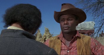 Movie still from “Buck and the Preacher” (1972), directed by Joseph Sargent – A man wearing a cowboy hat talking to another man in front of trees; Close Up shot, Over the shoulder angle