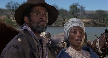 Movie still from “Buck and the Preacher” (1972), directed by Joseph Sargent – A man and a woman standing next to each other in front of a body of water; Medium shot, Low angle