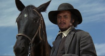 Movie still from “Buck and the Preacher” (1972), directed by Joseph Sargent – A man standing next to a horse in a field; Close Up shot, Low angle