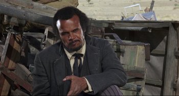 Movie still from “Buck and the Preacher” (1972), directed by Joseph Sargent – A man in a suit and tie sitting in a chair; Close Up shot, Low angle