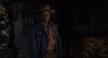 Movie still from “Buck and the Preacher” (1972), directed by Joseph Sargent – A man wearing a cowboy hat standing in front of a wall; Medium shot, Low angle