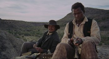 Movie still from “Buck and the Preacher” (1972), directed by Joseph Sargent – Two men sitting next to each other on a hill; Medium shot, Low angle