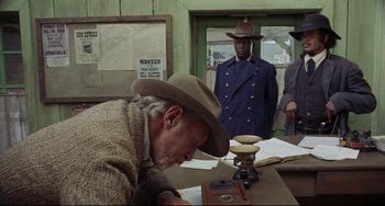 Movie still from “Buck and the Preacher” (1972), directed by Joseph Sargent – An old man in a cowboy hat writing on a desk; Medium shot, Low angle