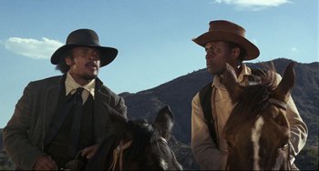 Movie still from “Buck and the Preacher” (1972), directed by Joseph Sargent – A couple of men standing next to each other on a horse; Medium shot, Low angle
