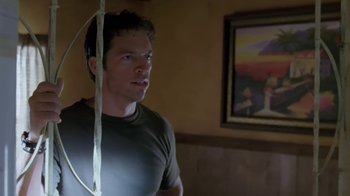 Movie still from “Bug” (2006), directed by William Friedkin – A man standing in front of a painting in a room; Medium shot, Low angle