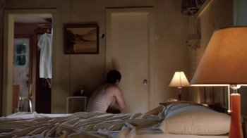 Movie still from “Bug” (2006), directed by William Friedkin – A person sitting on a bed in a room; Wide shot, High angle