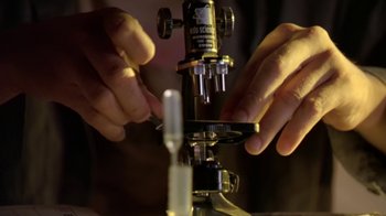 Movie still from “Bug” (2006), directed by William Friedkin – A person working on a microscope in a dark room; Extreme Close Up shot, Overhead angle