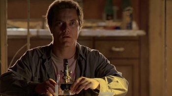 Movie still from “Bug” (2006), directed by William Friedkin – A man sitting at a table with a bottle in front of him; Close Up shot, Low angle