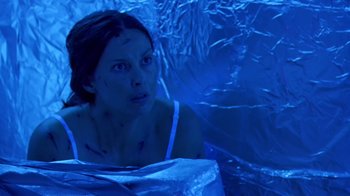 Movie still from “Bug” (2006), directed by William Friedkin – A woman in a white tank top is sitting in a room covered in foil; Medium shot, Overhead angle
