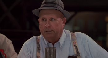 Movie still from “Bull Durham” (1988), directed by Ron Shelton – An older man wearing a hat and holding a microphone; Close Up shot, Over the shoulder angle