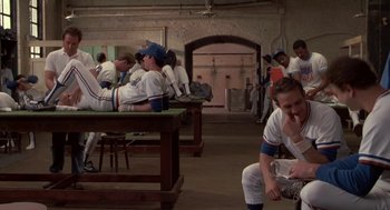 Movie still from “Bull Durham” (1988), directed by Ron Shelton – A baseball player sitting on a bench with other baseball players in the background; Wide shot, Over the shoulder angle