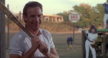Movie still from “Bull Durham” (1988), directed by Ron Shelton – A man standing in a field holding a baseball bat; Close Up shot, Over the shoulder angle